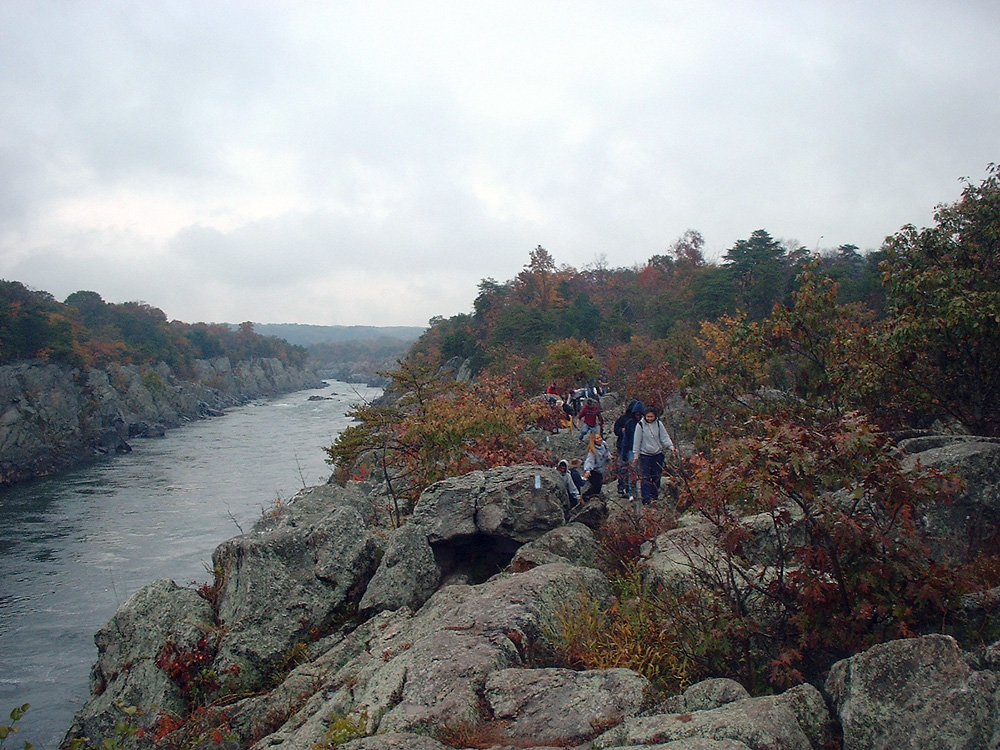 People hiking on big boulder rocks by a river Billy Goat Trail in Virginia.