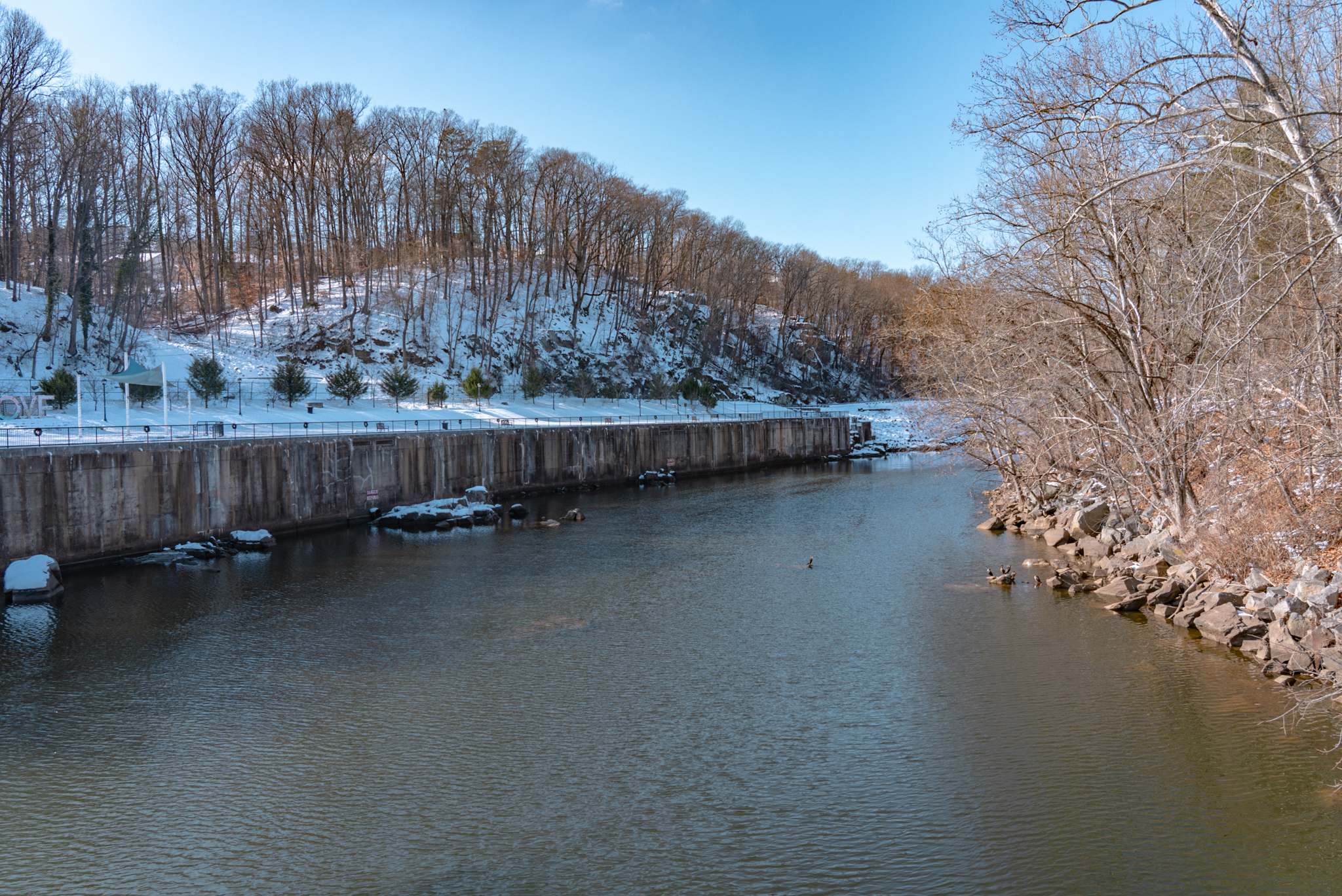 A river with ducks surrounded by trees and snow-covered hills in Occoquan, Virginia.