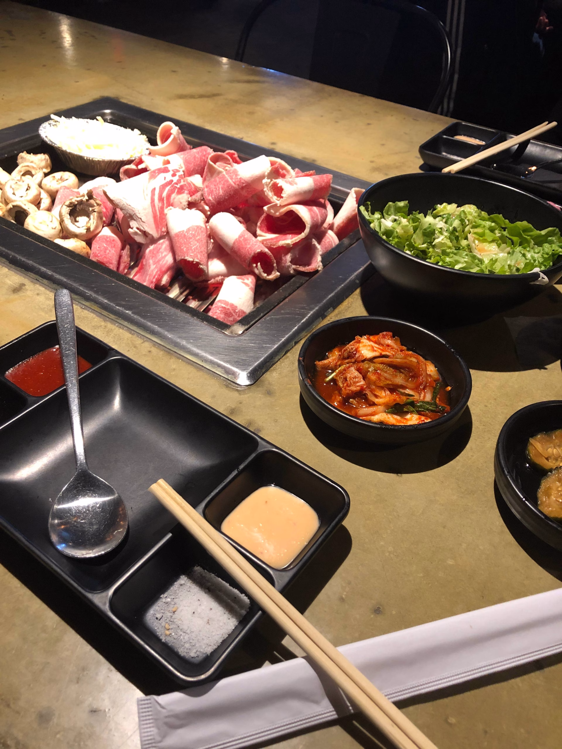 Meat on a grill with side dishes and sauces in separate containers on a table.