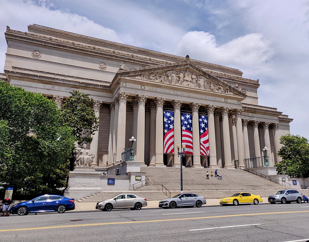 The National Archives Museum building in Washington DC with cars parked on the side of the road.