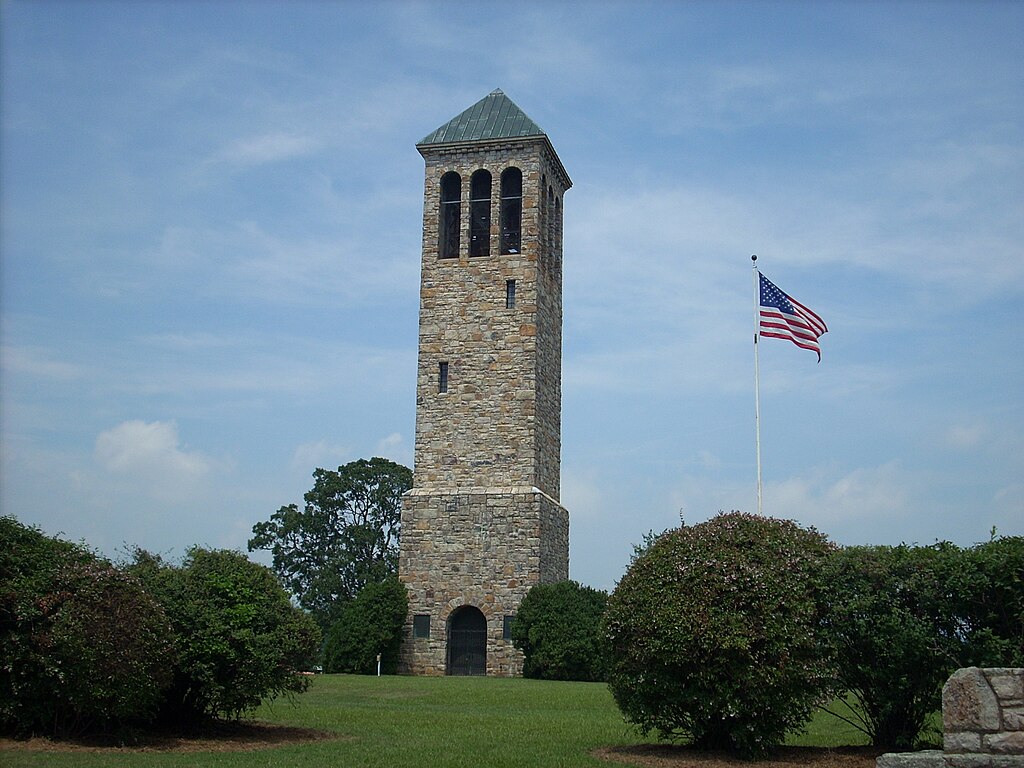 A stone tower in Virginia surrounded by bushes and a USA flag.
