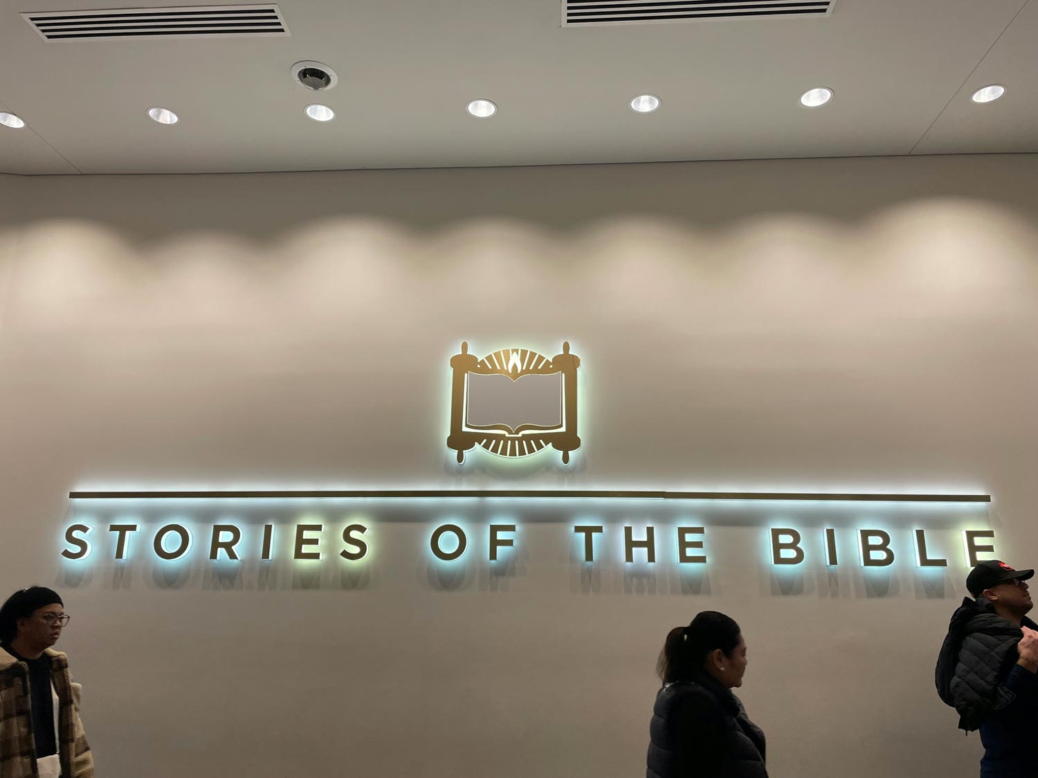 People walking past a figure of a book on a wall with the text "stories of the bible".