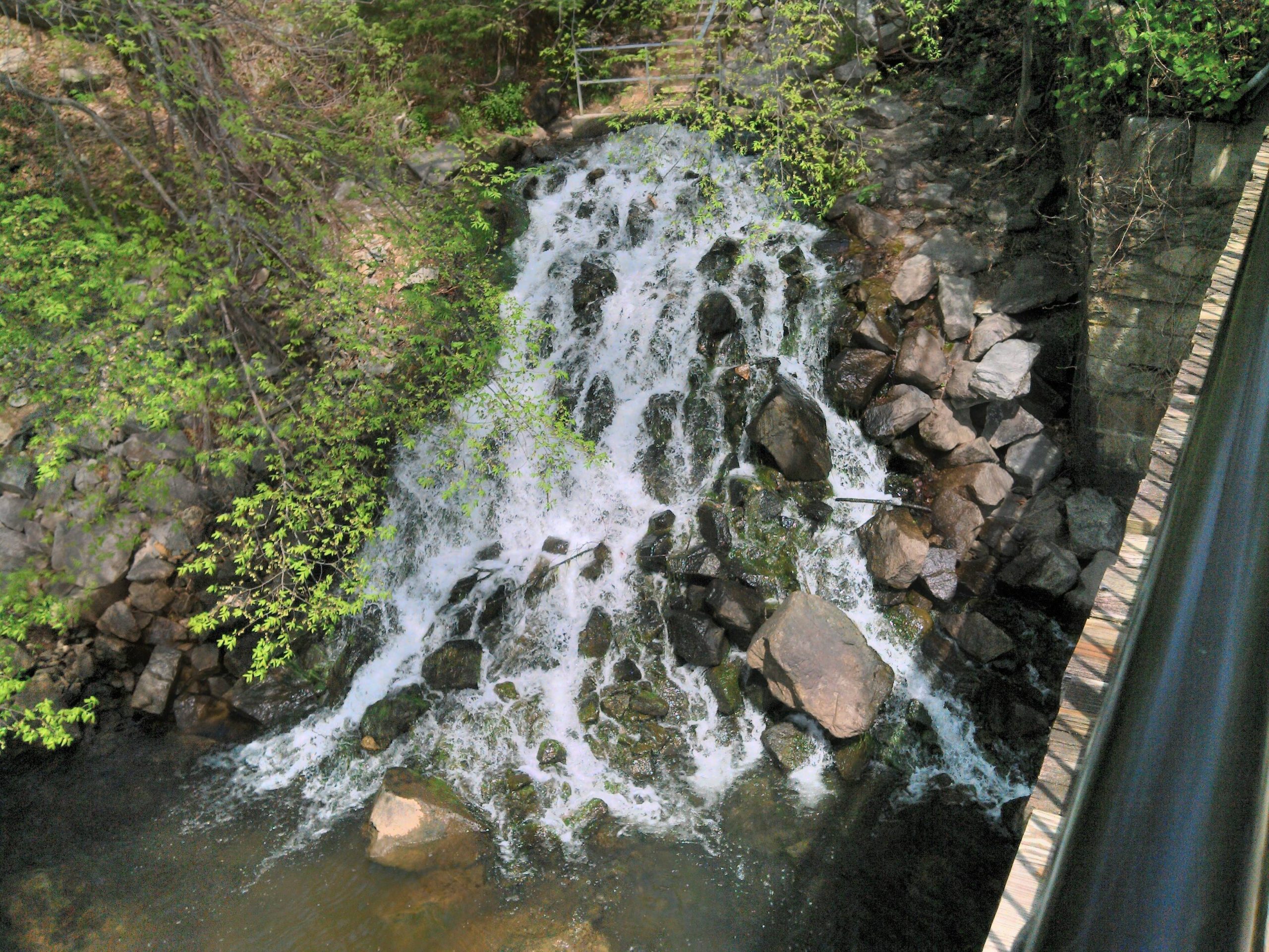 A bird's eye view of a mini waterfall with big rocks.