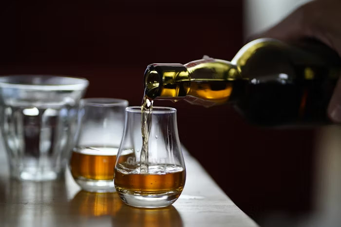 Drink being poured from a glass bottle to a glass cup.