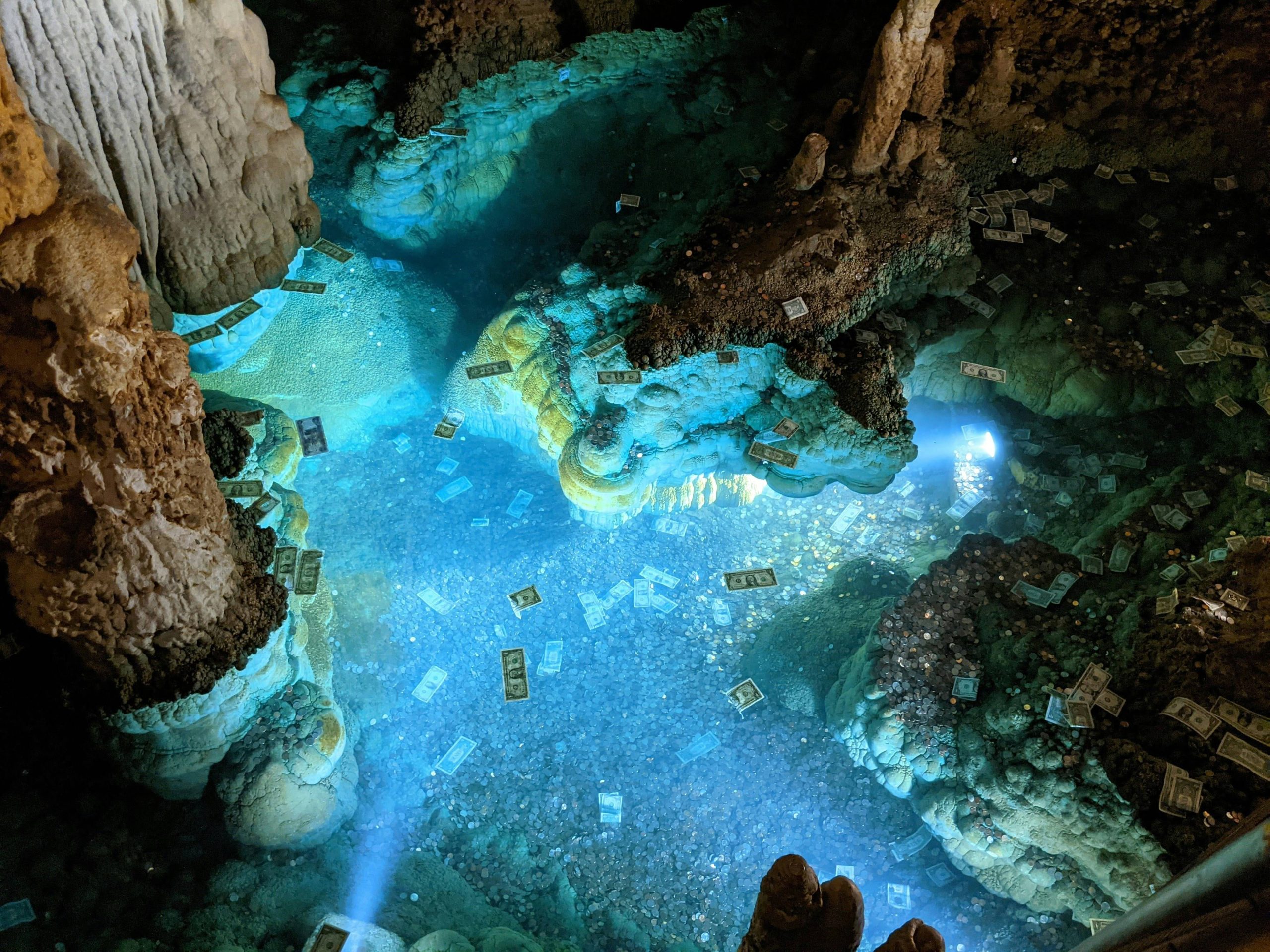 A lower part of a cave illuminated with blue light and with rocks, coins, and bills.