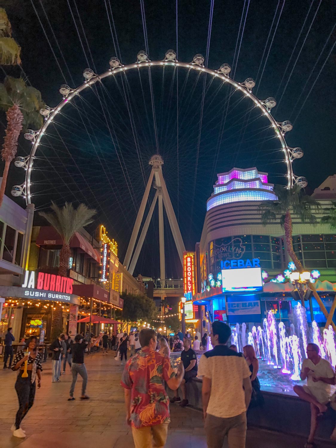 People walking on The LINQ Promenade with a view of the roller coaster in the back.