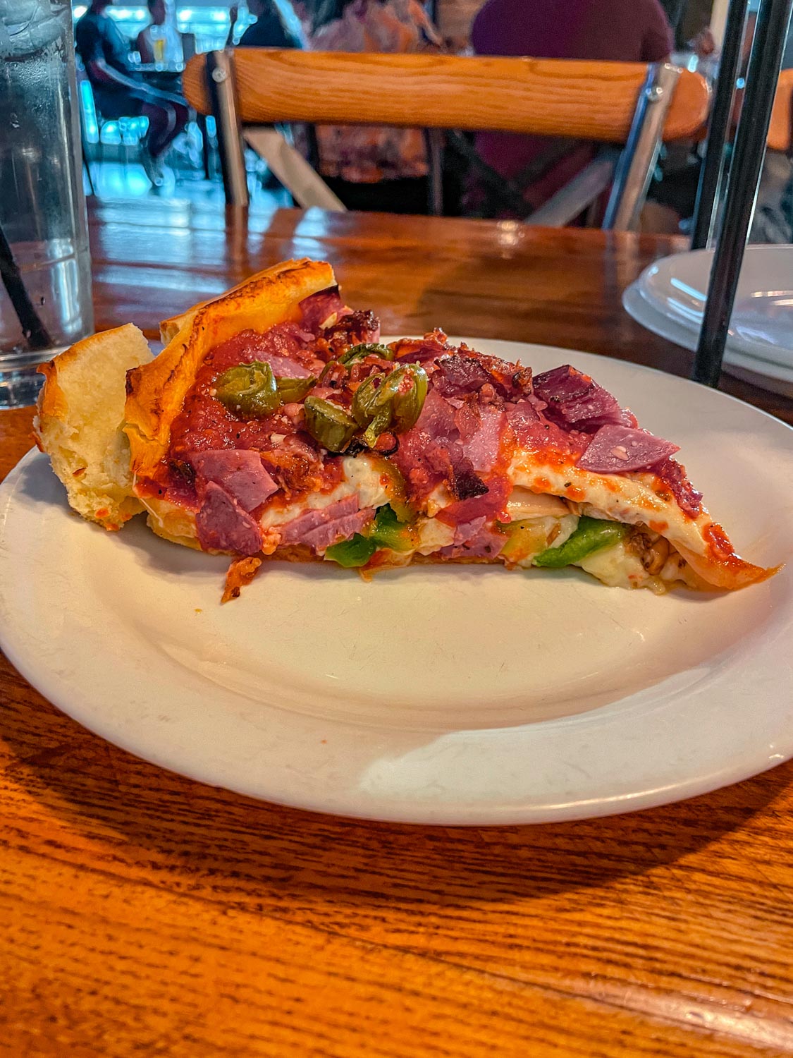 A slice of pizza on a white plate on a wooden table.