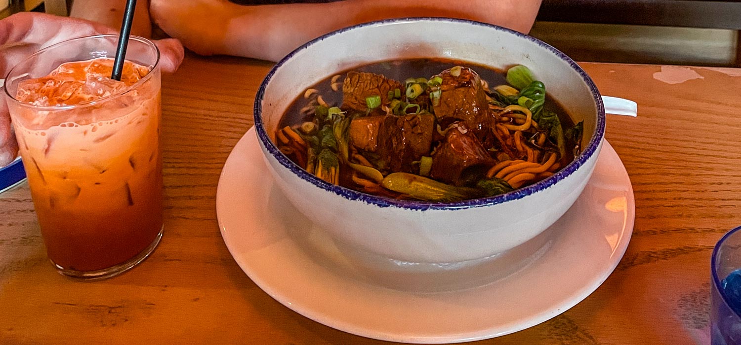 A bowl of beef noodle and a cup of iced milk tea or coffee.