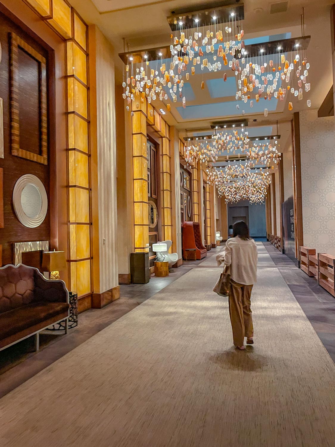 A woman walking inside a fancy hallway of one of the best hotels on the Las Vegas Strip with carpeted floors, chandeliers, and luxurious furniture.