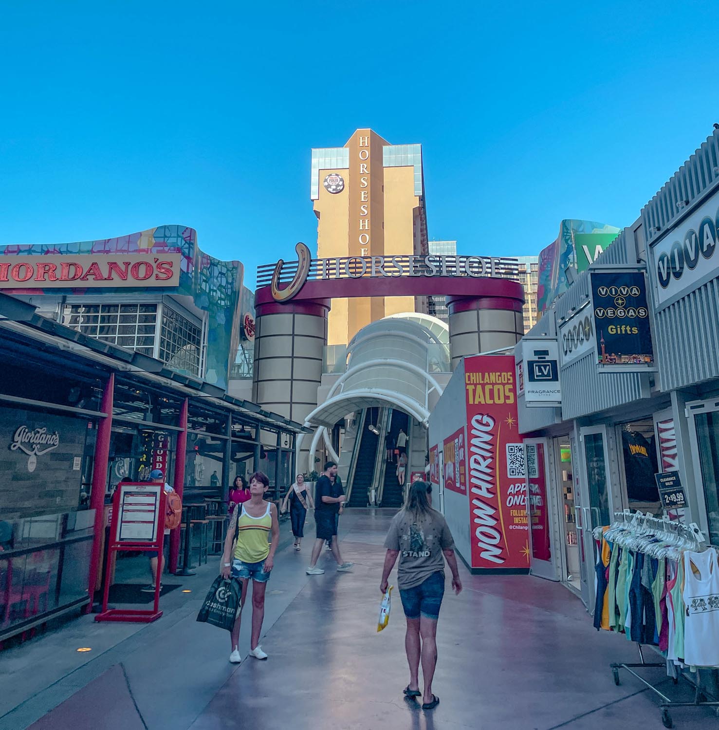 Outdoor shopping area with an outdoor elevator leading to the Horseshoe Las Vegas Hotel building.