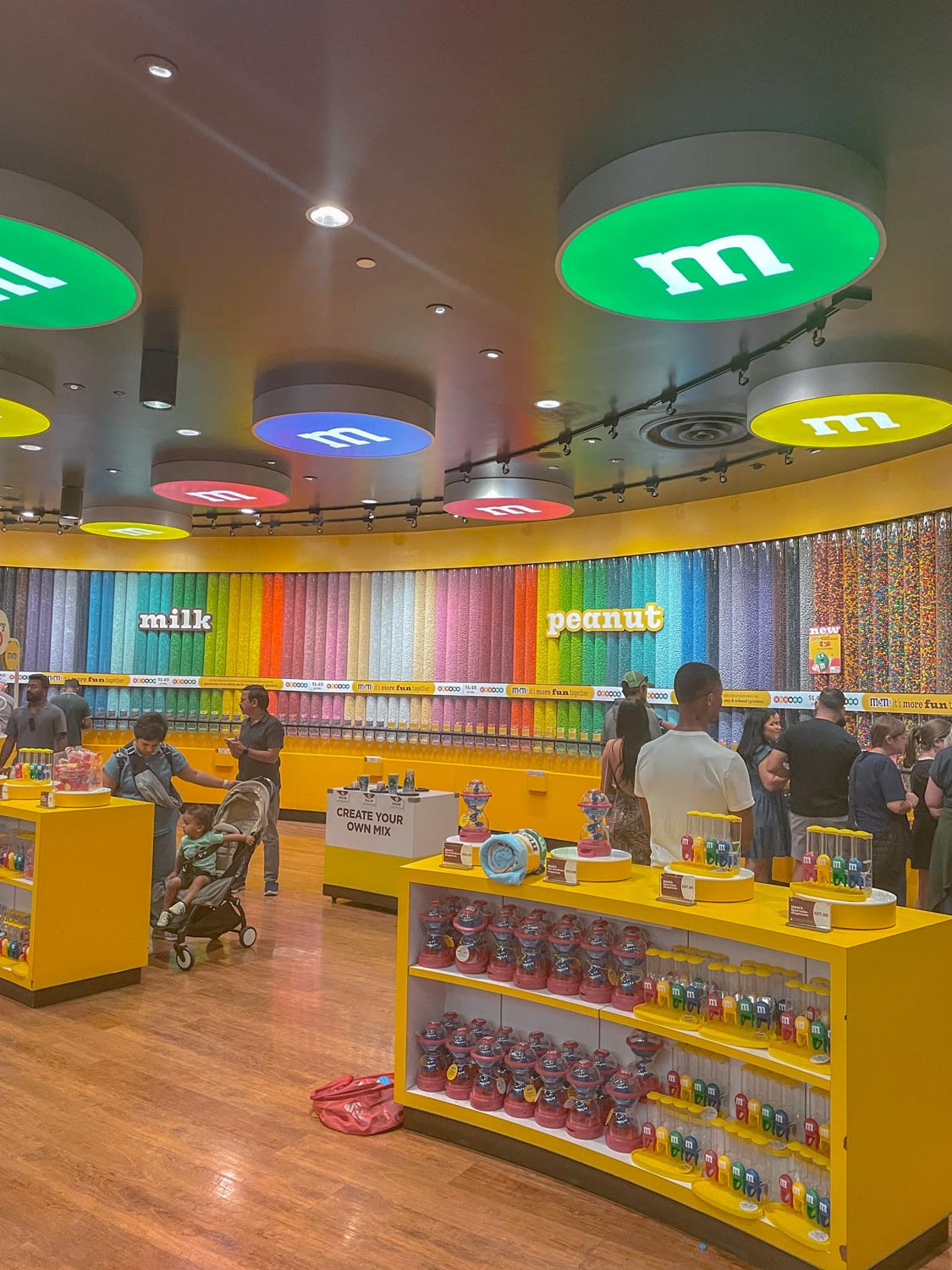 People inside the M&M’s World with yellow walls and various candy containers and products.