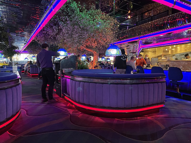 The inside of Peppermill Restaurant and Fireside Lounge in Las Vegas with neon lights and a tree near a table.