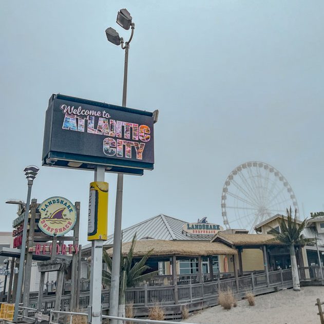 A sign that says "Welcome to Atlantic City" sign near a restaurant and ferris wheel.