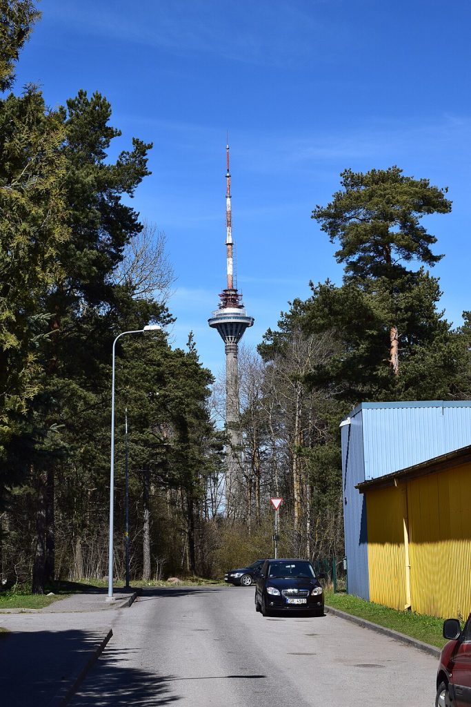Cars passing by a road surrounded by trees and a view of the Tallinn TV Tower.