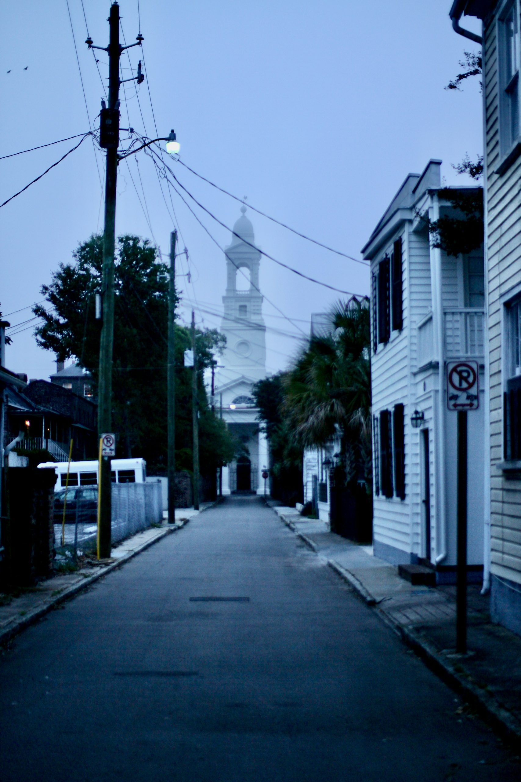 An empty street in Charleston, South Carolina at night with a view of a church tower.
