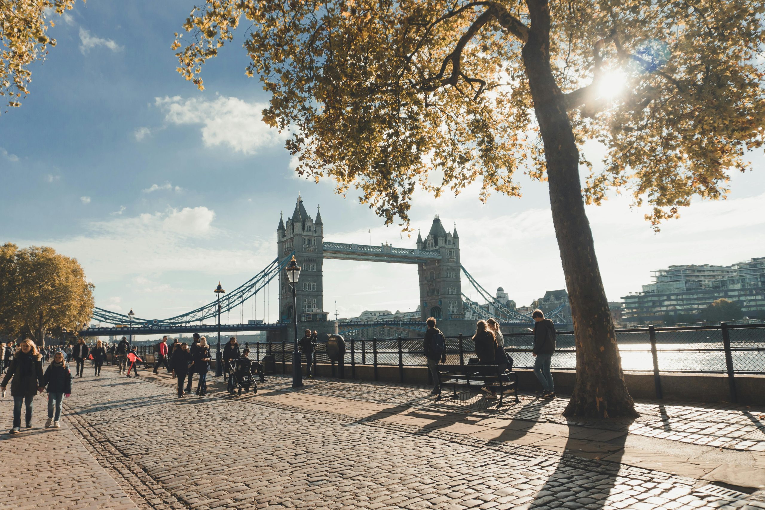 People walking on the river side of London with a view of the bridge.