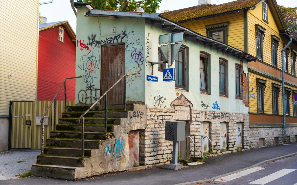 A building, on the side of the road, with graffiti and stairs to its door at a neighborhood in Tallinn, Estonia.