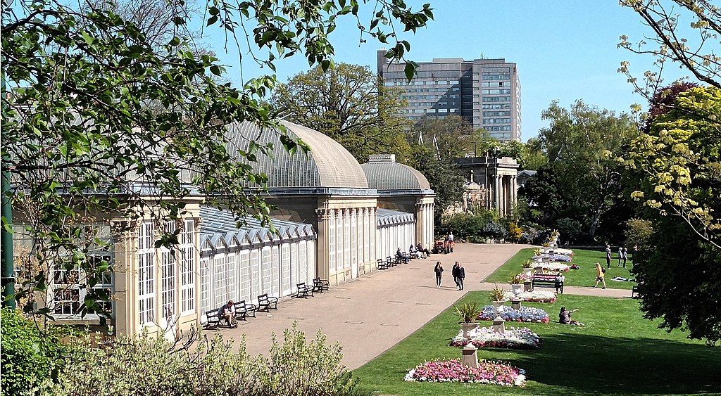 A botanical garden in Sheffield with glass pavilions, lawns with flowers, and trees on a sunny day.