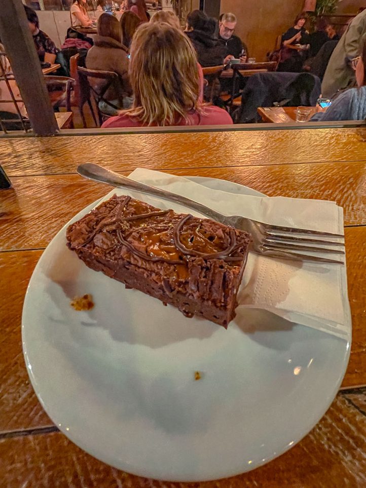 Salted caramel brownie on a white plate with fork and tissue on a table.