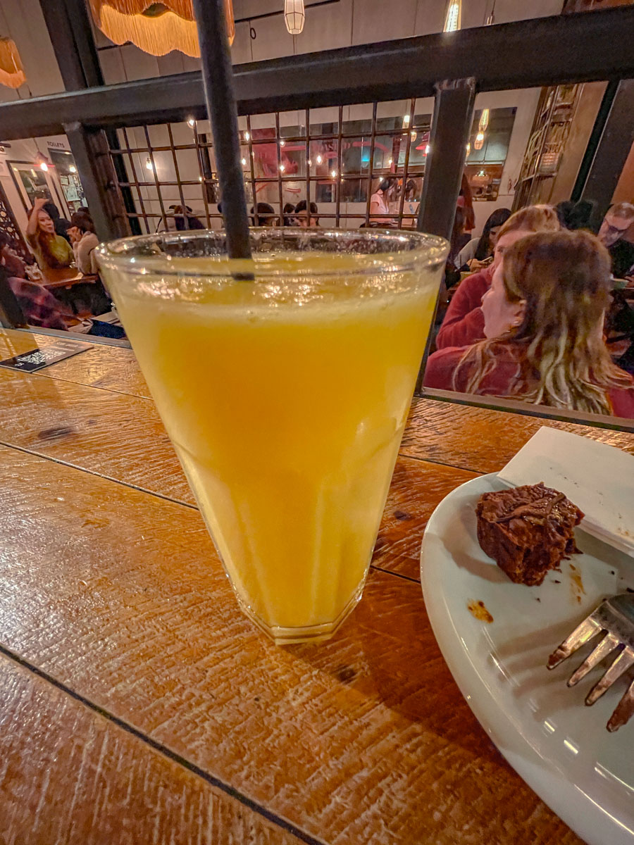 A glass of mango passionfruit smoothie with black straw on a table.
