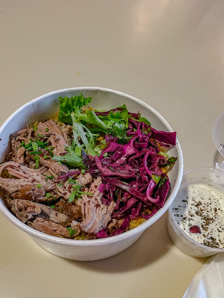 Meat and vegetable dish in a paper bowl with dressing on the side.