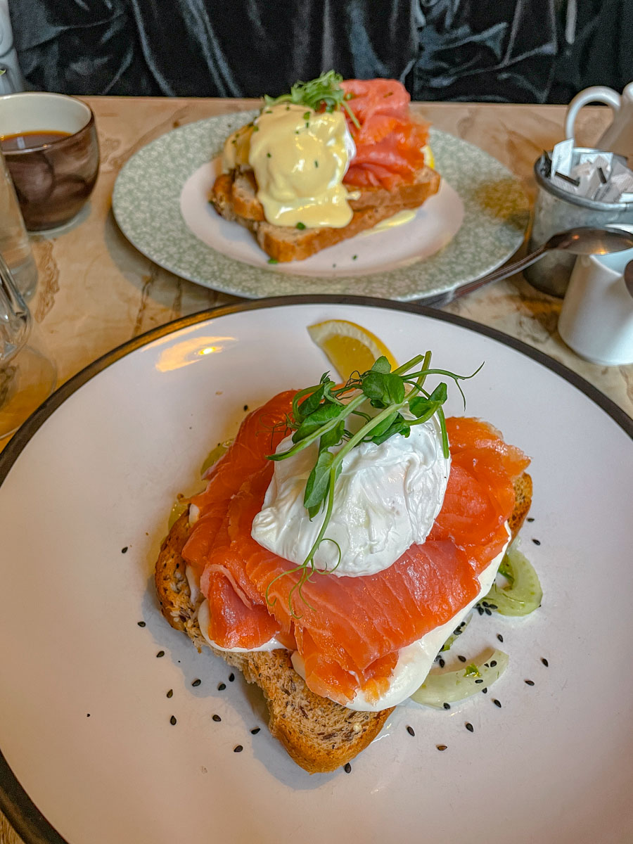 A toast on a plate topped with egg, salmon slice, and green garnish.