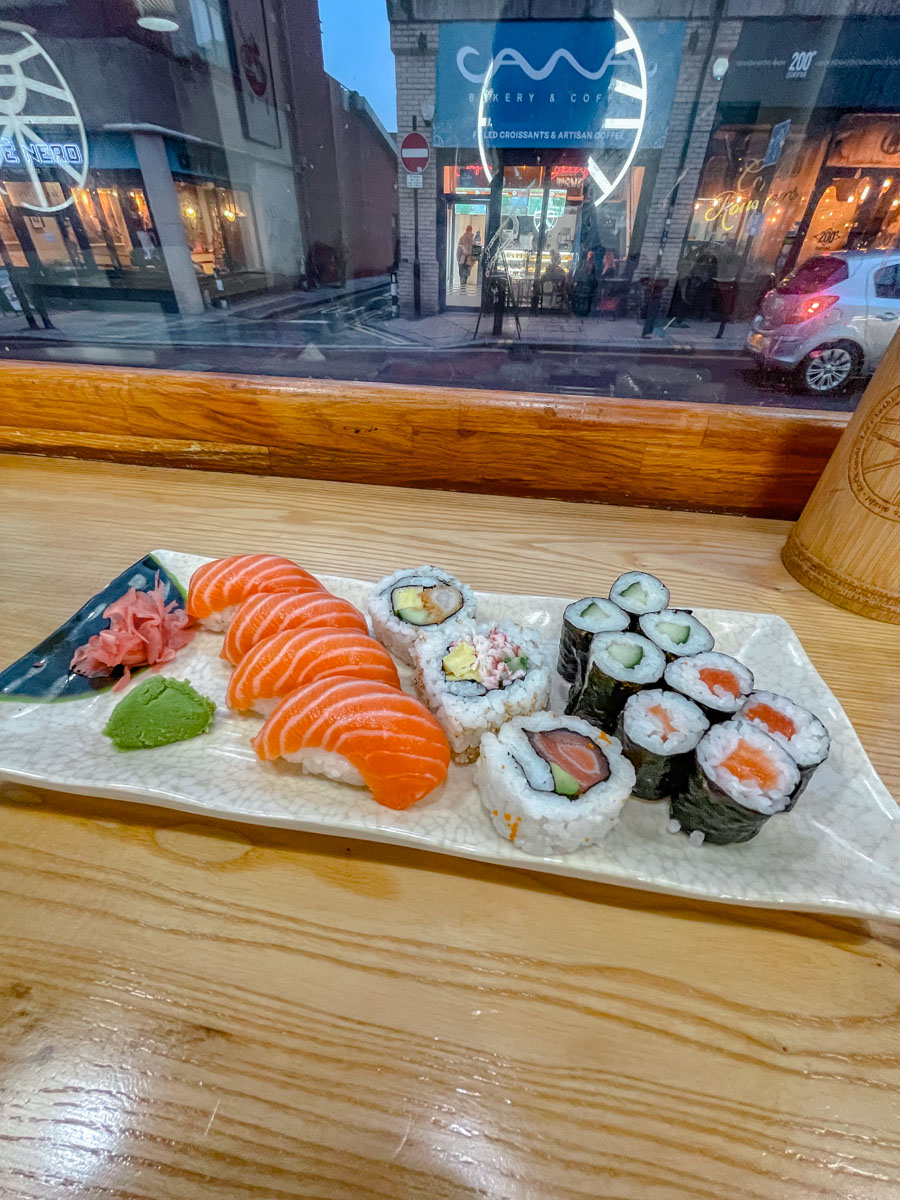 A rectangular plate of various sushi and maki with wasabi on a wooden table by the window inside a restaurant in Sheffield, UK.