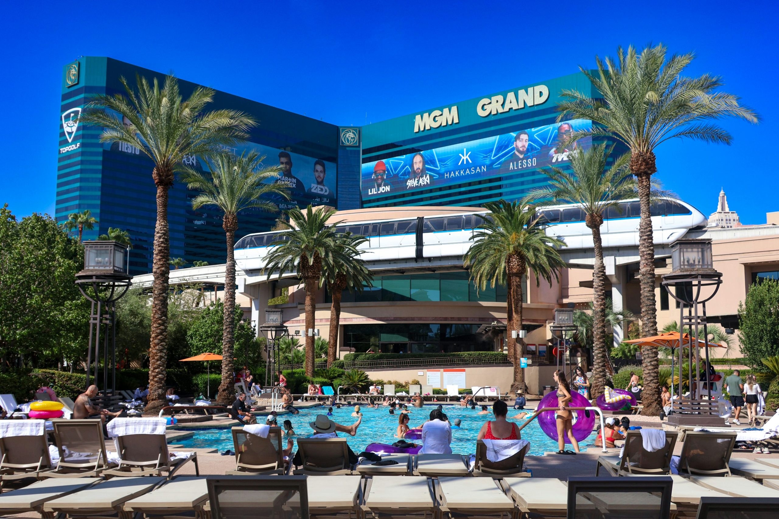 People hanging out at a Las Vegas hotel swimming pool with palm trees.