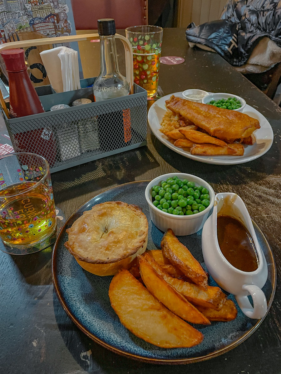 Plate of fried potatoes, pies, green peas, and gravy on a table inside a pub in Sheffield.