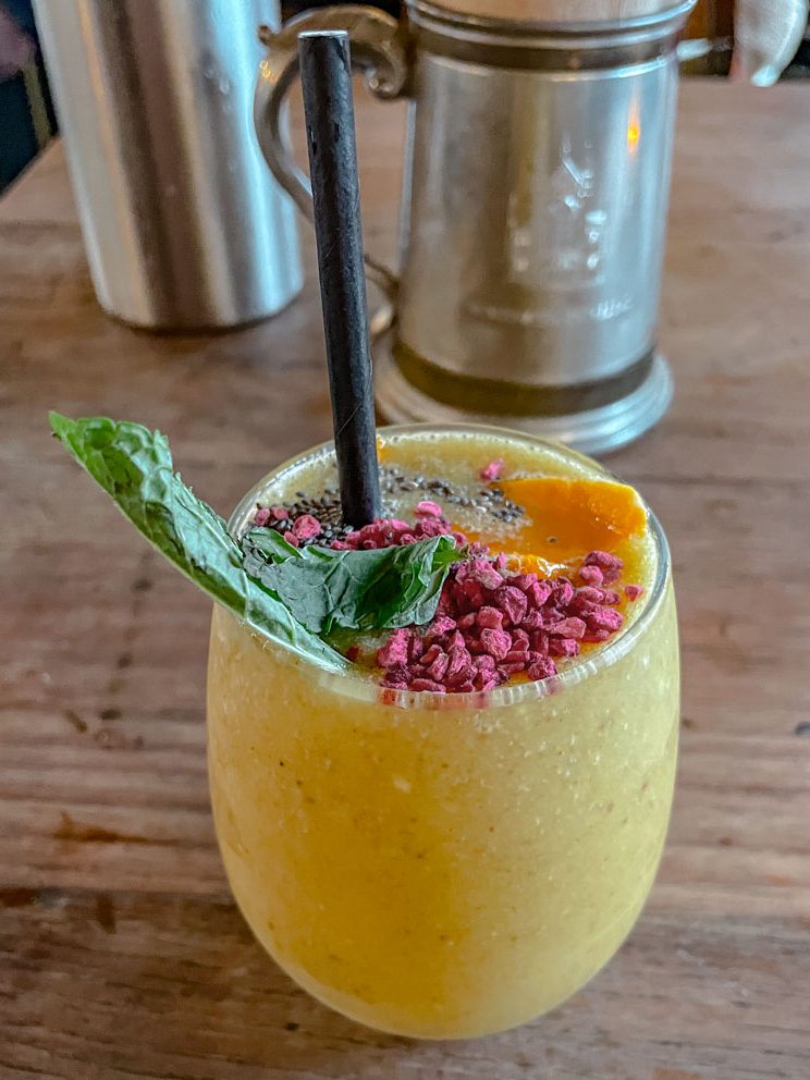 A glass of fruit juice on a table with colorful garnish and black straw.