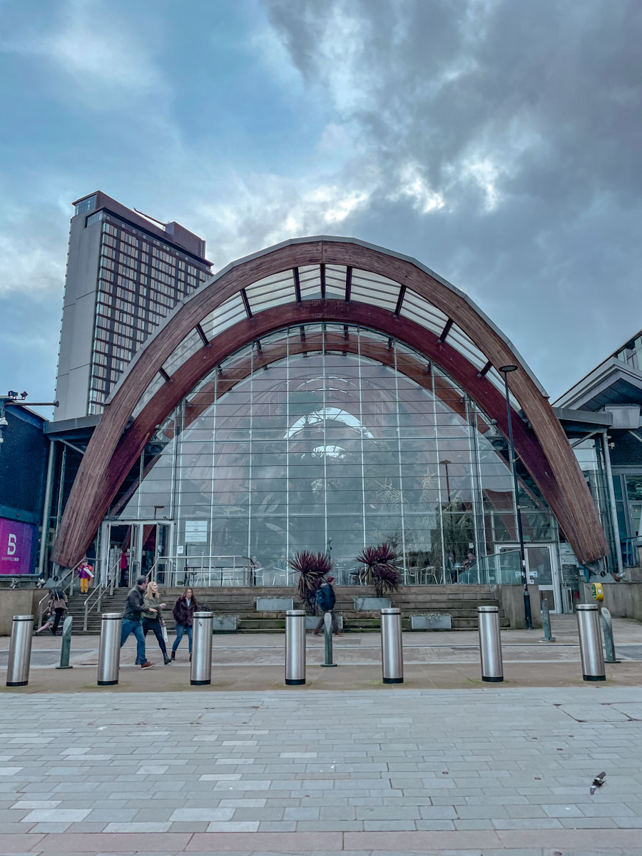 People walking on the sidewalk in front of an indoor garden glasshouse  in Sheffield.