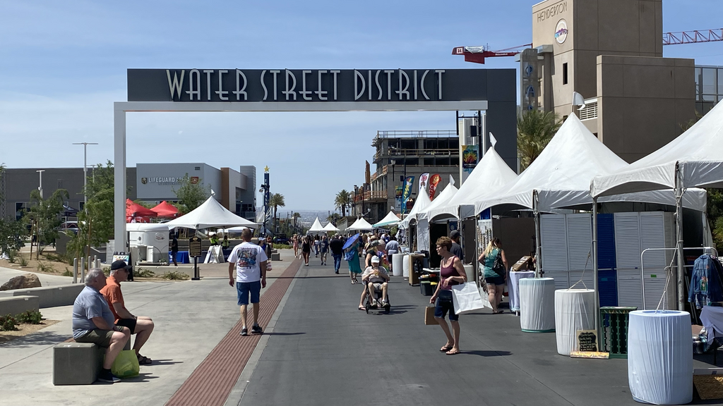 People sitting on benches and walking near the arch that says "Water Street District" in Henderson, Nevada.