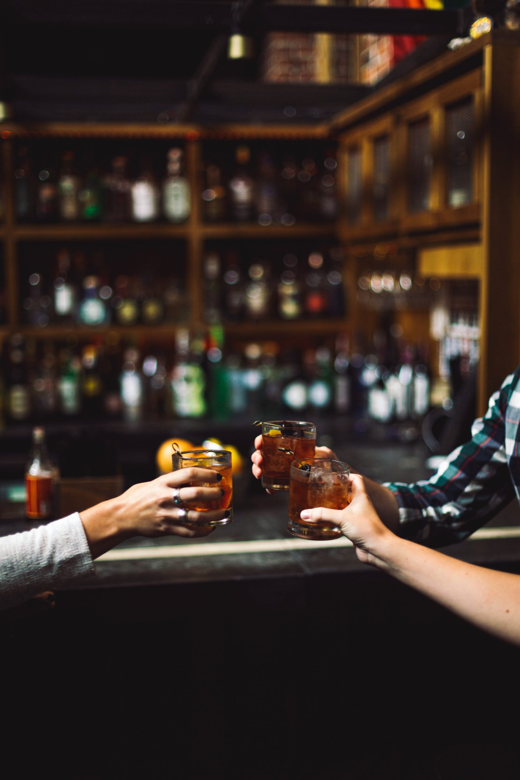 Arms of three people, each holding out clear drinking glasses at a bar.