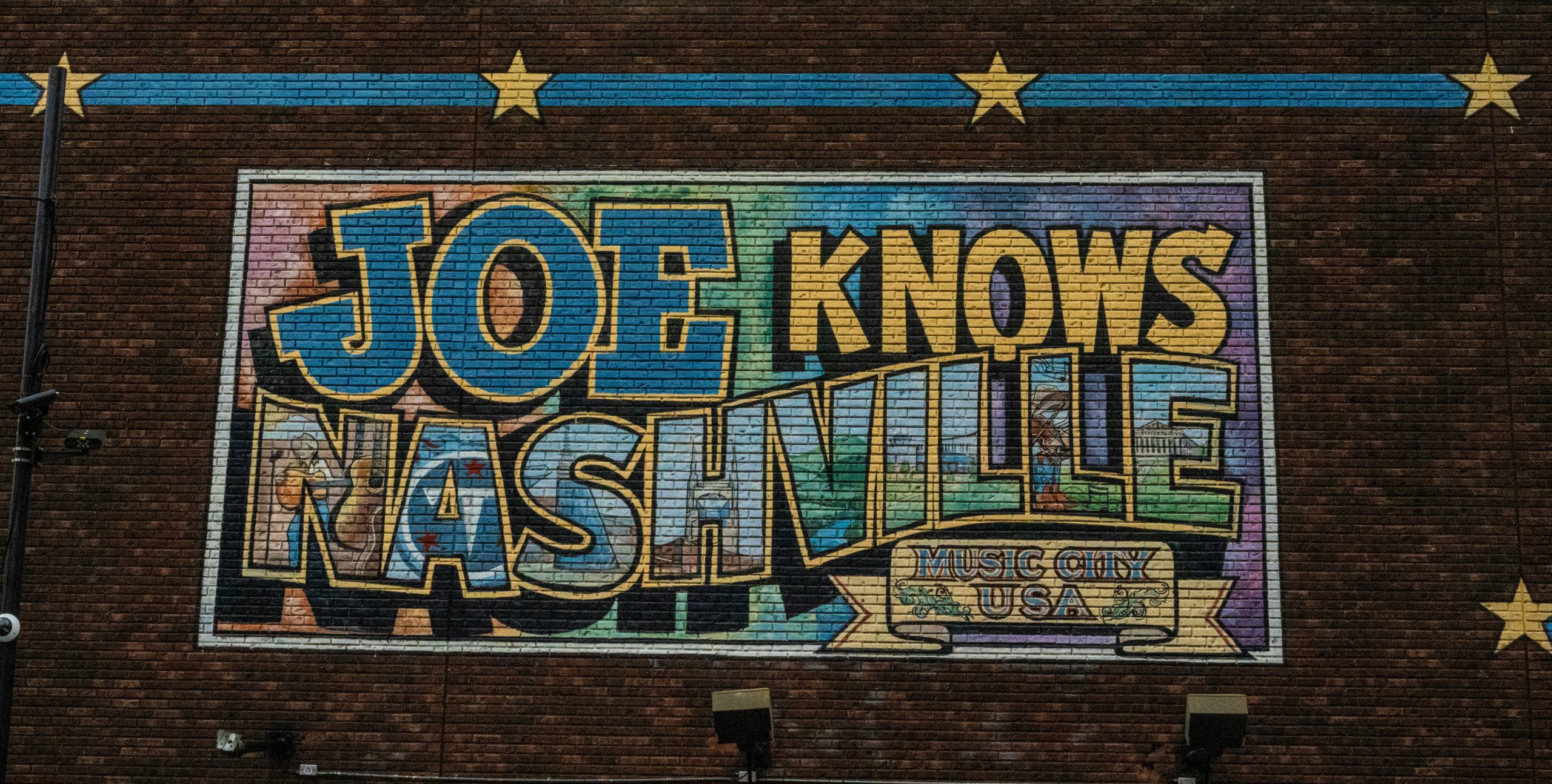 A colorful mural with text that says "Joe Knows Nashville Music City USA" at night.