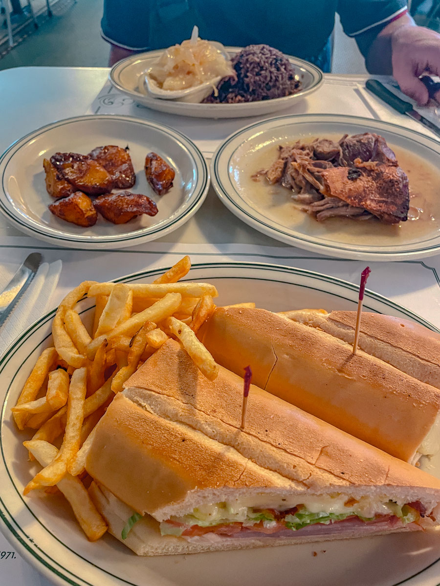 Sandwiches, fries, and meat on plates on a table at a restaurant.