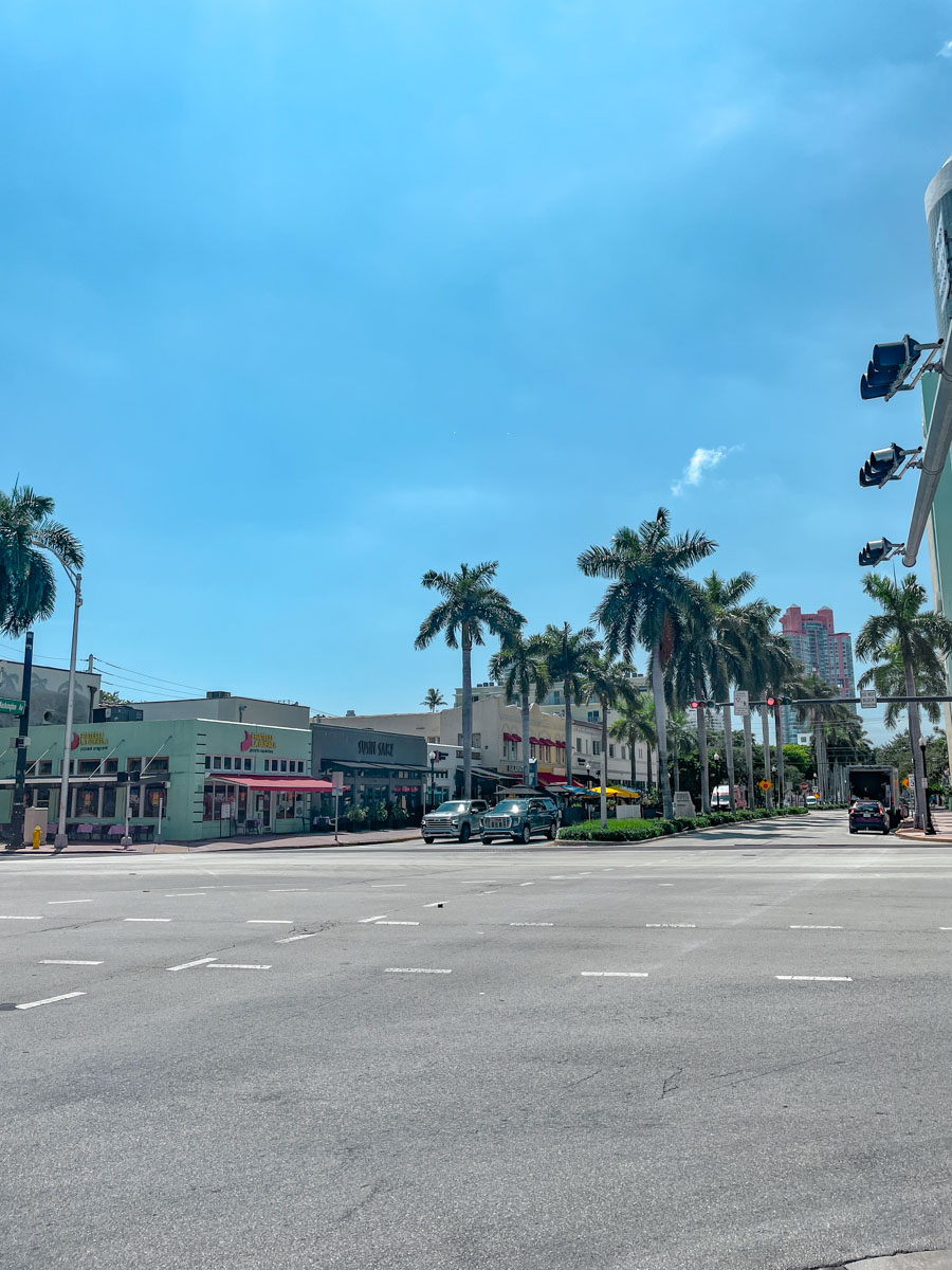 An intersection in Miami with cars and palm trees on a sunny day.