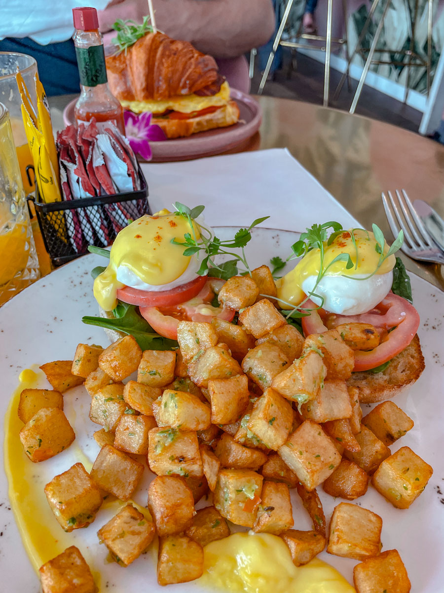 Eggs Benedict and fried potatoes and croissant on plates on a table.