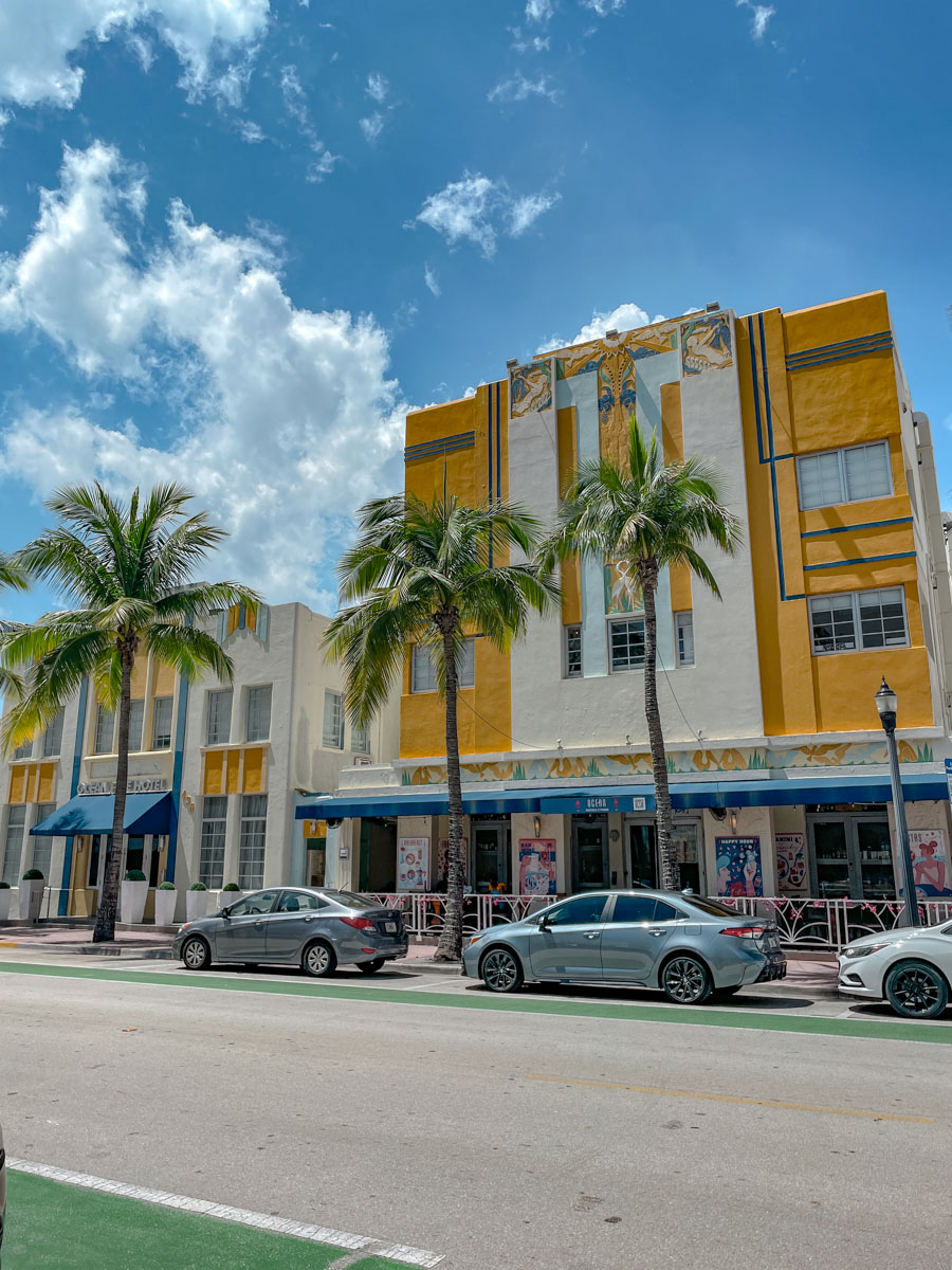 Cars parked on the side of a road in Miami lined with palm trees along colorful buildings.