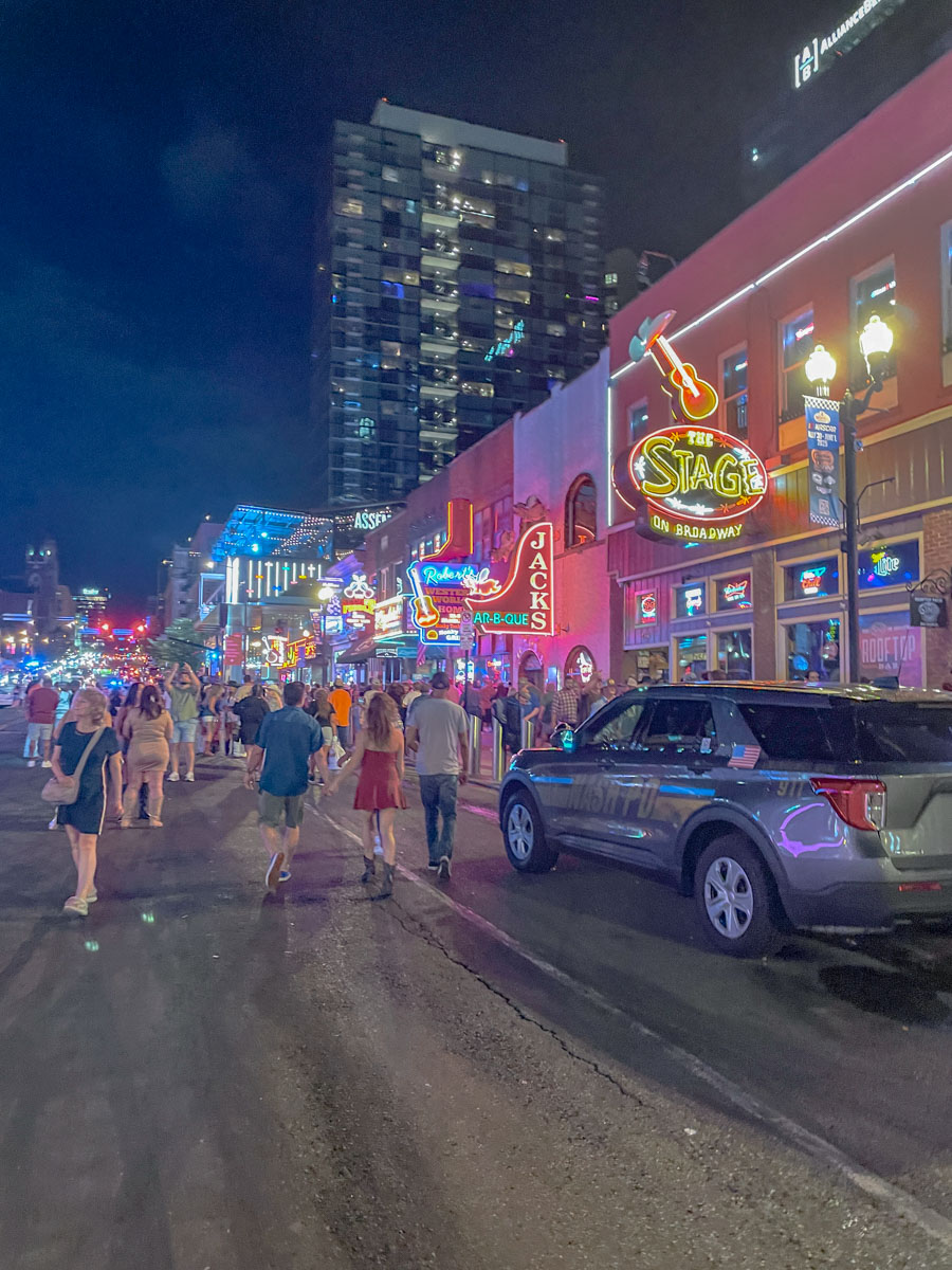 People walking on Broadway street in Nashville with bar signs light up.