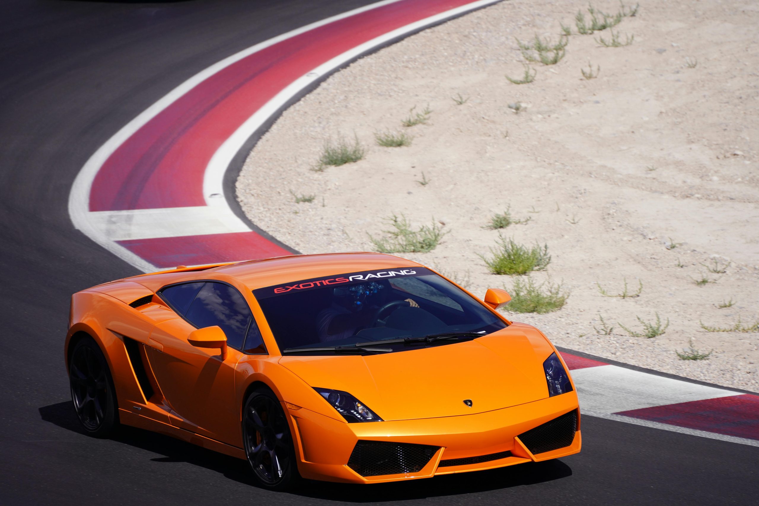An orange sports car racing on a desert racing track.