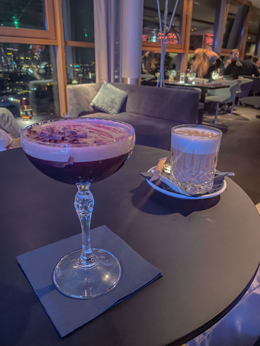 Fancy drinks on a black round table at a hotel bar on its top floor at night.