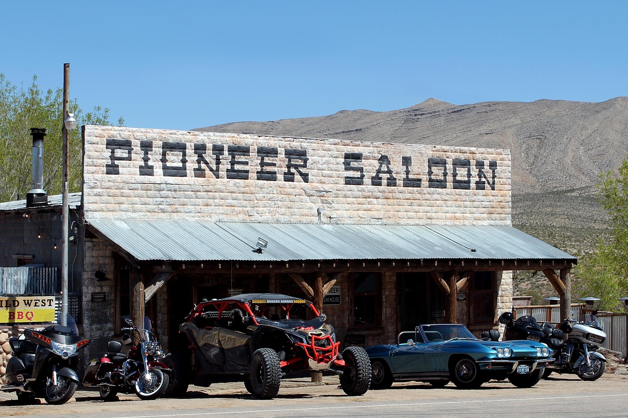 The outside of Pioneer Saloon with cars and motorcycles parked in front and mountains at the back.