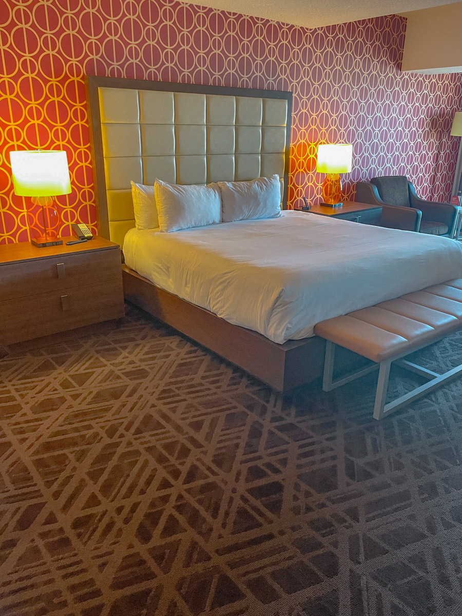 A hotel room with a bed, chair, tables, lamps, and carpeted floor and wall Horseshoe Las Vegas Hotel.