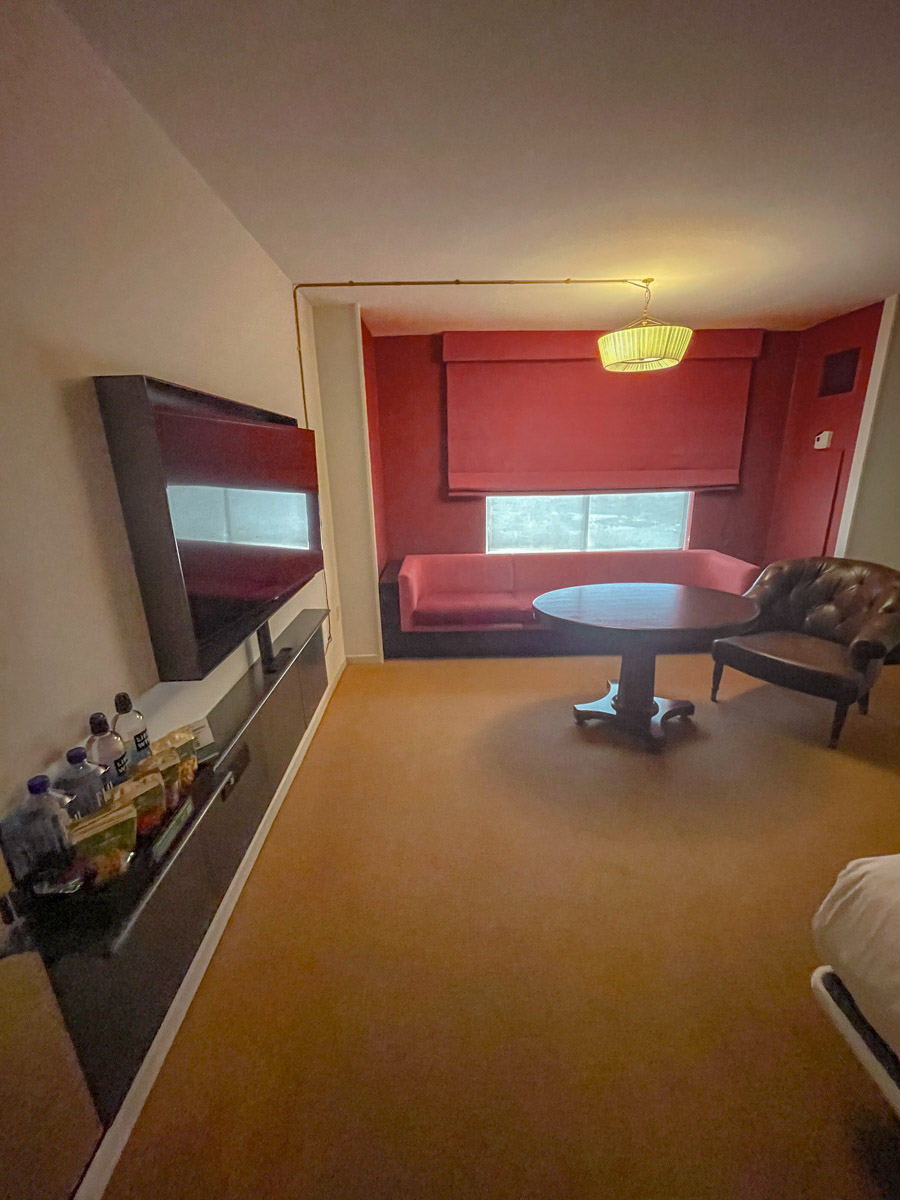 Inside a carpeted hotel room with TV, couch, table, and chair.