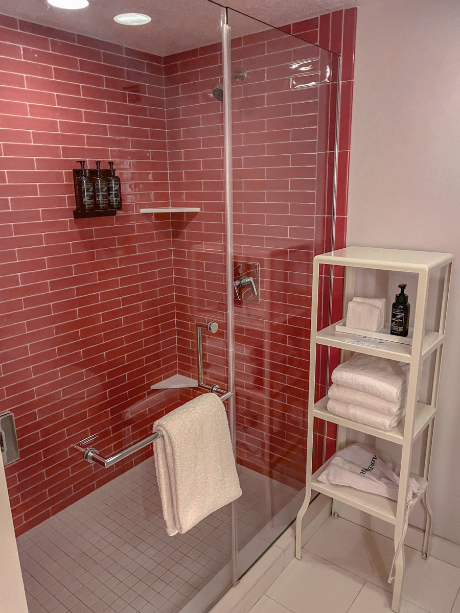 Inside hotel bathroom with shower, towels, shelves, and toiletries in Park MGM Las Vegas.