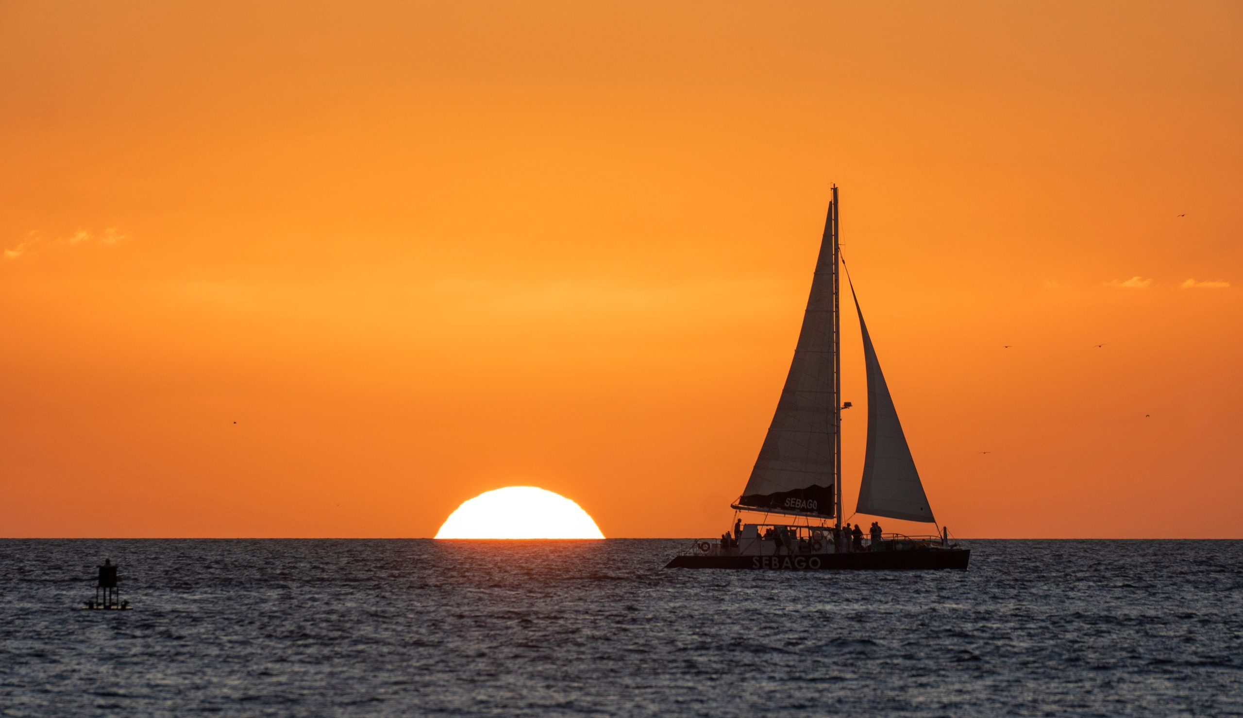 The sun setting and a yacht on water with orange sky in the background in Key West, Florida.