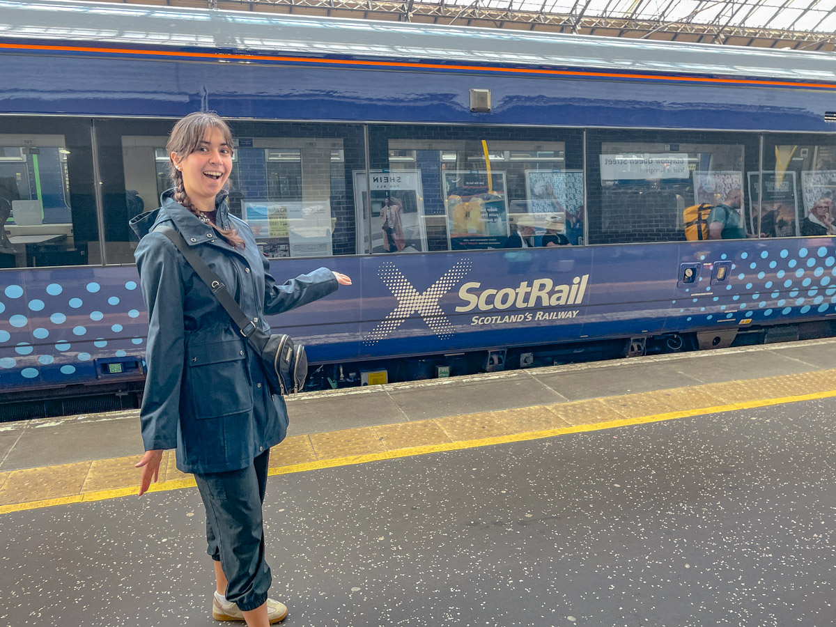 A woman standing on a train platform in front of a ScotRail train.