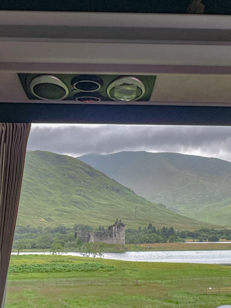Scottish highlands castle, lake, and mountains as seen from a van window.