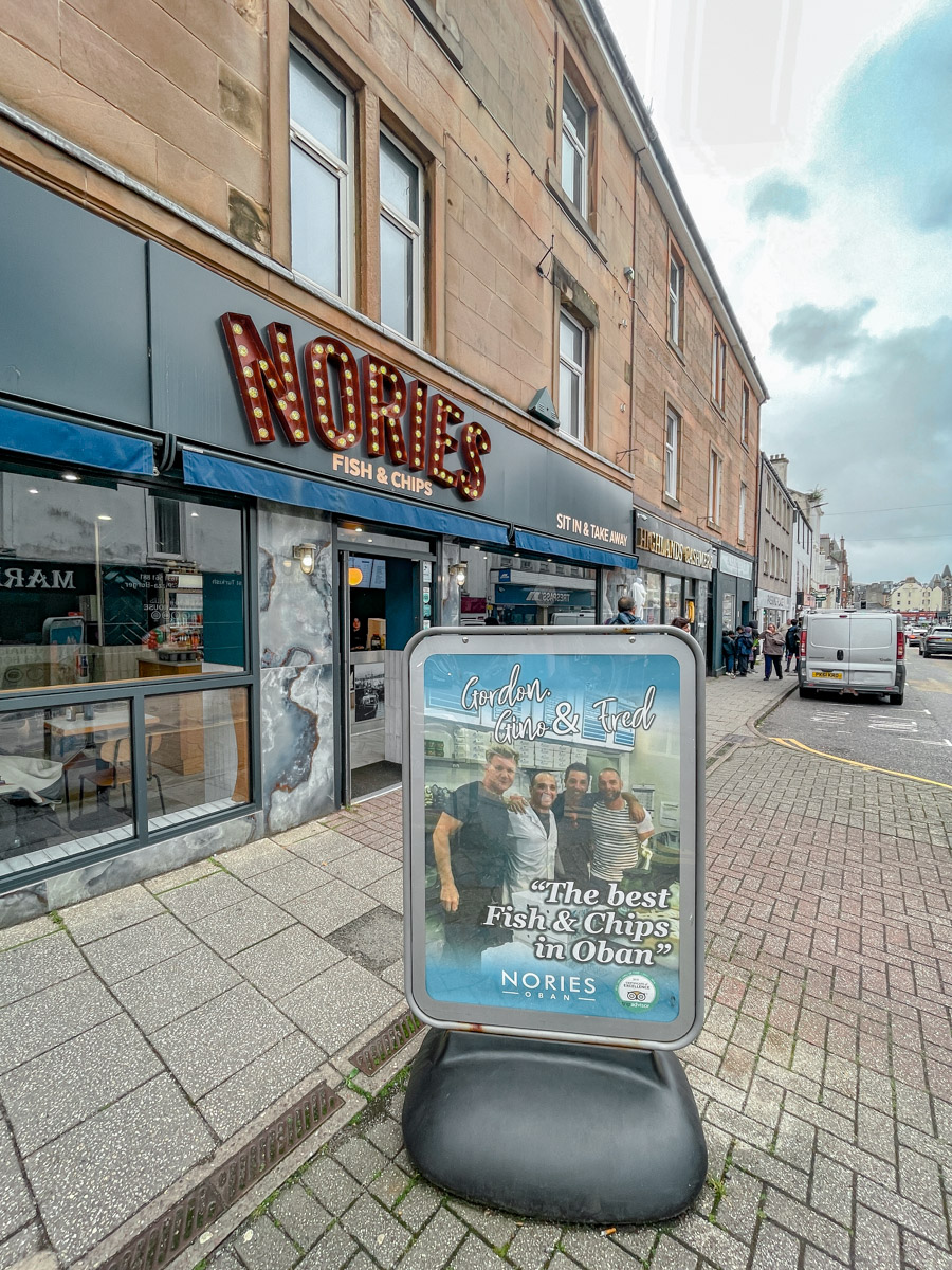 Storefront of a restaurant in Oban, Scotland with a photograph of 3 men as an poster displayed in front.