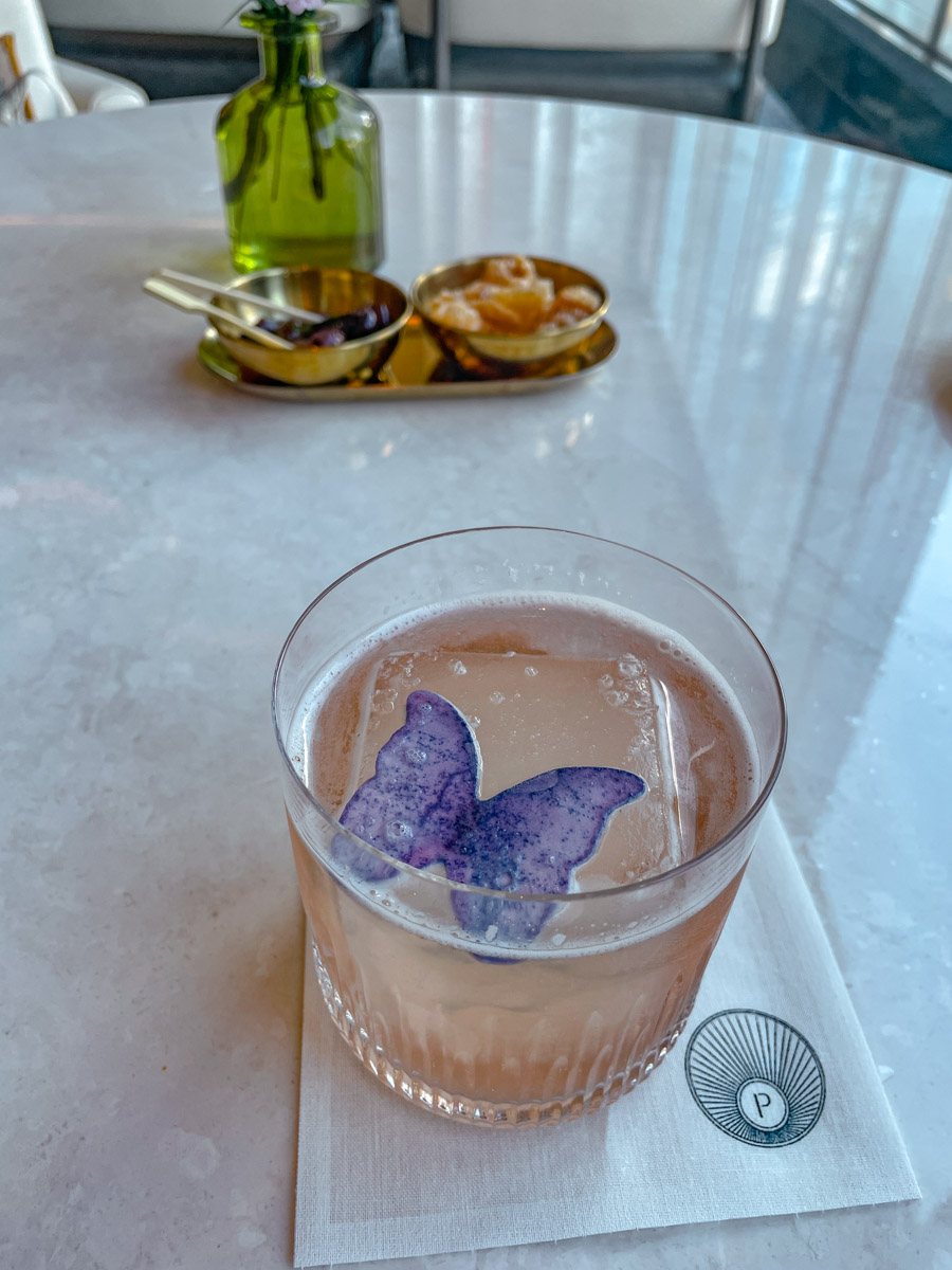 Mocktail in a glass with a purple butterfly shaped garnish.